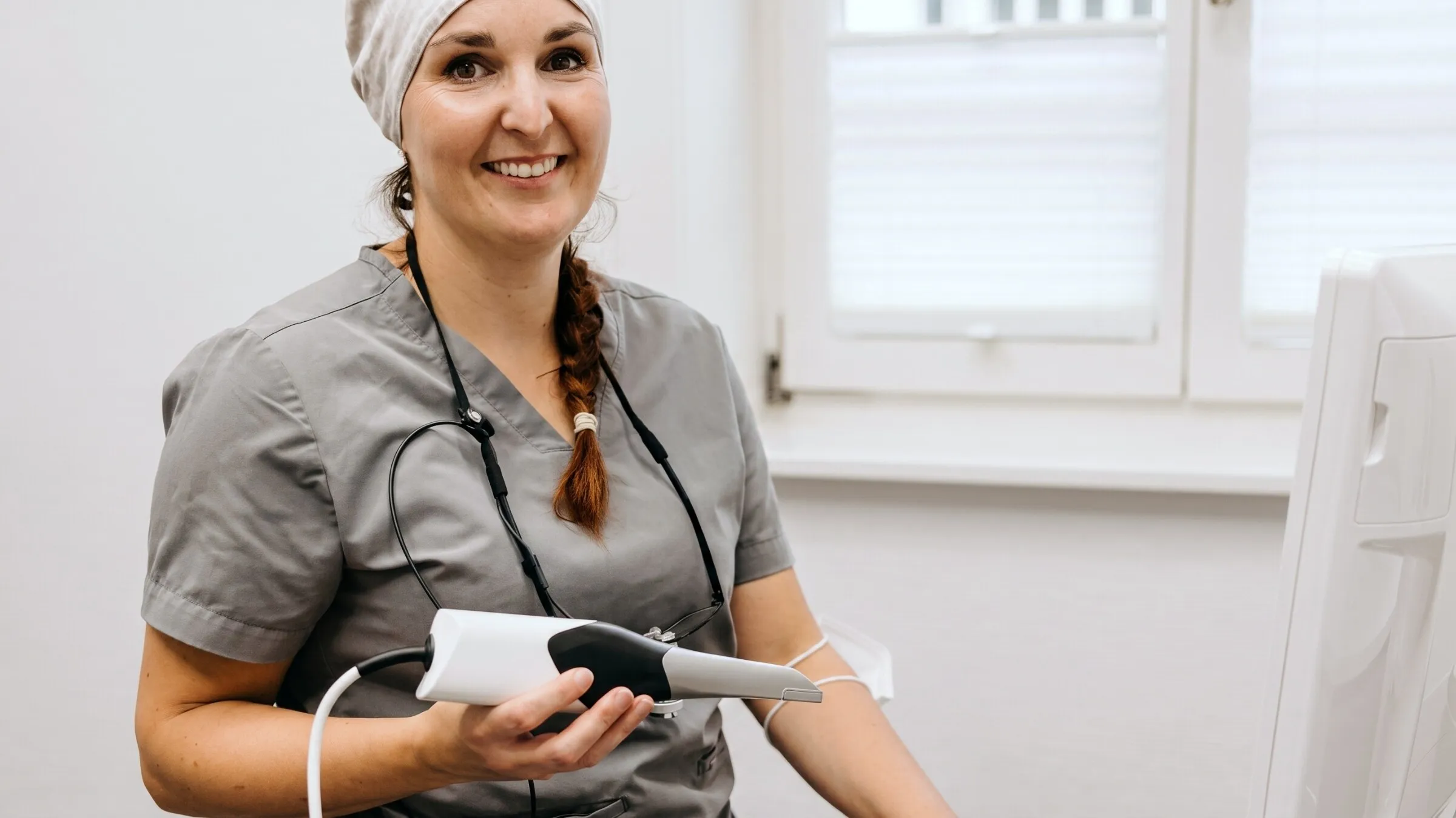 Zahnärztin hält das Handstück des Intraoralscanners neben der Scanner-Einheit.
